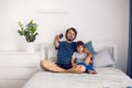 bearded father and son are sitting on the bed in T-shirts and watching football match on TV. a man holds a remote