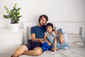 bearded father and son are sitting on the bed in T-shirts and watching football match on TV. a man holds a remote