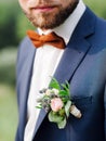 Bearded groom in a blue suit with a red bow tie and a boutonniere of dried flowers and tender roses. Groom`s boutonniere closeup.