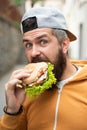 Bearded guy eats fast food. Burger is not helpful food. Very hungry guy. Hunger Man eat Hamburger outdoor. Man eat tasty Royalty Free Stock Photo