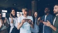 Bearded guy with expressive face is making wish and blowing candles on birthday cake while his colleagues are clapping