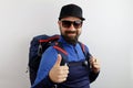 Bearded hiker with a backpack, sunglasses and hat, success sign doing positive gesture with hand, thumbs up similing and happy.