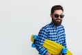 Bearded hipster in checkered shirt holding yellow skateboard