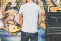 Bearded hipster man dressed in white t-shirt is stands against wall with graffiti. Mock up. Space for logo, text, image. Royalty Free Stock Photo