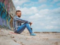 Bearded hipster man with mohawk sits on a concrete pier near the sea and looks into the distance against the sky and clouds Royalty Free Stock Photo