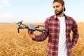Bearded hipster man shows small compact drone and holds remote controller in his hand. Farmer agronomist looks at