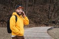 Bearded hipster man tourist in yellow hoodie and cap stands outdoors, talking on mobile phone. Smiling man calling friends