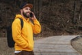 Bearded hipster man tourist in yellow hoodie and cap stands outdoors, talking on mobile phone. Smiling man calling friends