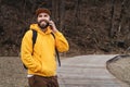 Bearded hipster man tourist in yellow hoodie and cap stands outdoors, talking on mobile phone. Smiling man calling friends