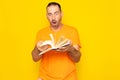 Bearded Hispanic man in his 40s turning the pages of a book visibly excited, isolated on yellow studio background.