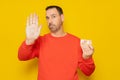 Bearded hispanic man in his 40s wearing a red jumper holding a 10 euro banknote and making the stop sign isolated over