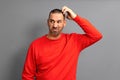 Bearded Hispanic man in red sweater frowning and looking dissatisfied while scratching his head, standing over blue Royalty Free Stock Photo
