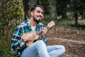 Bearded Hispanic man wearing flannel singing while playing ukulele under a tree Royalty Free Stock Photo