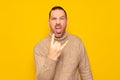 Bearded hispanic man wearing turtleneck isolated over yellow background showing rock gesture with fingers and sticking