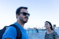 Bearded husband with sunglasses and rucksack and happy wife exploring, traveling and looking for directions, standing with groom