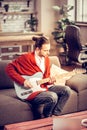 Bearded instrumentalist sitting on sofa and playing the guitar