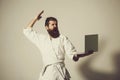Bearded shouting karate man in kimono with laptop Royalty Free Stock Photo