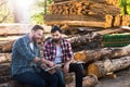 bearded lumberjacks sitting on logs with axe and digital tablet
