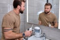 Bearded male casually dressed using oral dental irrigator with in bathroom near mirror