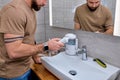 Bearded male casually dressed using oral dental irrigator with in bathroom near mirror