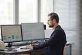 Bearded male engineer using computer with blueprints on screen in office