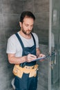 Bearded male plumber making notes in clipboard while checking shower