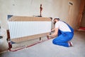 Bearded male worker installing radiator in apartment.