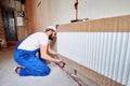 Bearded male worker installing radiator in apartment.
