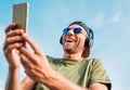 Bearded man in baseball cap, wireless headphones and blue sunglasses found something funny in smartphone device and cheerful