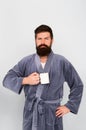 Bearded man in bathrobe with mug. Breakfast concept. Man with beard in blue bathrobe enjoy morning coffee or tea. Guy in