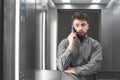 Bearded man with a beard stands in the elevator, speaks by telephone and looks at the camera. Portrait of an office worker in the Royalty Free Stock Photo