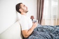 Bearded man in bed drinking morning coffee in sunrise light at home Royalty Free Stock Photo