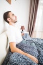 Bearded man in bed drinking morning coffee in sunrise light at home Royalty Free Stock Photo