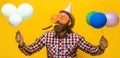 Bearded man in birthday hat and funny glasses with balloons blowing noisemaker. Party time. Holiday.