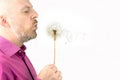 Bearded man blowing on a dandelion flower. Flying dandelion seeds