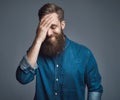 Bearded man in blue denim shirt with hand on head