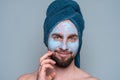 A bearded man with a blue towel on his head and a cosmetic mask on his face. Cosmetology procedures for men. Skin care for men