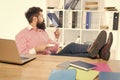 Bearded man with brutal look relax at work desk drinking coffee in modern office, hipster