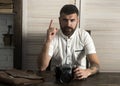 Bearded man with camera and raised finger up at desk