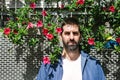 Bearded man in casual attire leaning on a flowered wall while looking camera Royalty Free Stock Photo