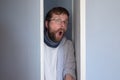 Bearded man in casual clothes is hiding in a closet, he peeps through the open door and looks in surprise with an open