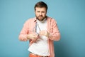 Bearded man cleans glasses, wiping them with a shirt and squinting, looking confidently into the camera.