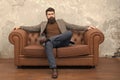 Bearded man with confident face sit leather couch. Loft interior apartment. Businessman realtor work. Furniture shop