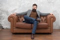 Bearded man with confident face sit leather couch. Loft interior apartment. Businessman realtor work. Furniture shop