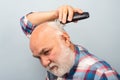 Bearded man cutting his own hair with a clipper. Man hair treatment. Gray man hair clippings. Bald man hairclipper