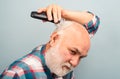 Bearded man cutting his own hair with a clipper. Man hair treatment. Gray man hair clippings. Bald man hairclipper