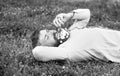 Bearded man with daisy flowers in beard lay on grassplot, grass background. Man with beard on calm face sniffs dandelion