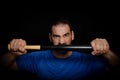 Bearded man dressed in blue t-shirt in defiant pose posing whit a baseball bat on black background Royalty Free Stock Photo