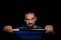 Bearded man dressed in blue t-shirt in defiant pose posing whit a baseball bat on black background Royalty Free Stock Photo