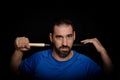 Bearded man dressed in blue t-shirt in defiant pose posing whit a baseball bat on black background Royalty Free Stock Photo